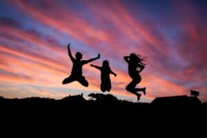 Three people jump for joy against the sunset after achieving health goals.