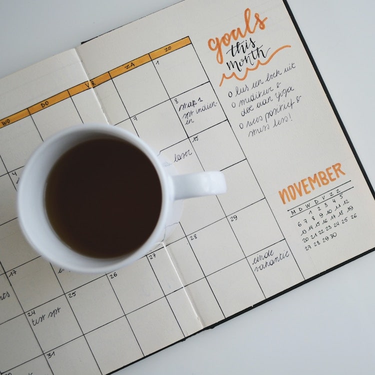 An agenda opened to a calendar with a cup of coffee on top