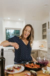 A woman sprinkling seasoning over a plate of food.