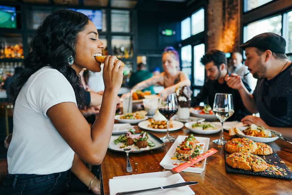 A woman biting into food at a dinner table with friends