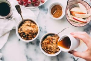 Someone pouring maple syrup, a natural sweetener, over a small bowl of oats