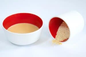 A bowl of savory tahini sauce next to a small bowl of sesame seeds on it's side