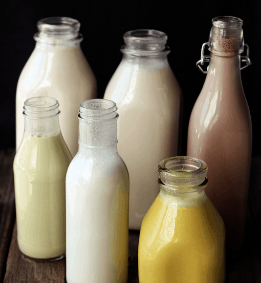 Various glass bottles filled with a variety of nut milk alternatives.