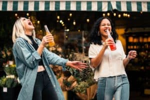 Two women smiling drinking soda from a bottle