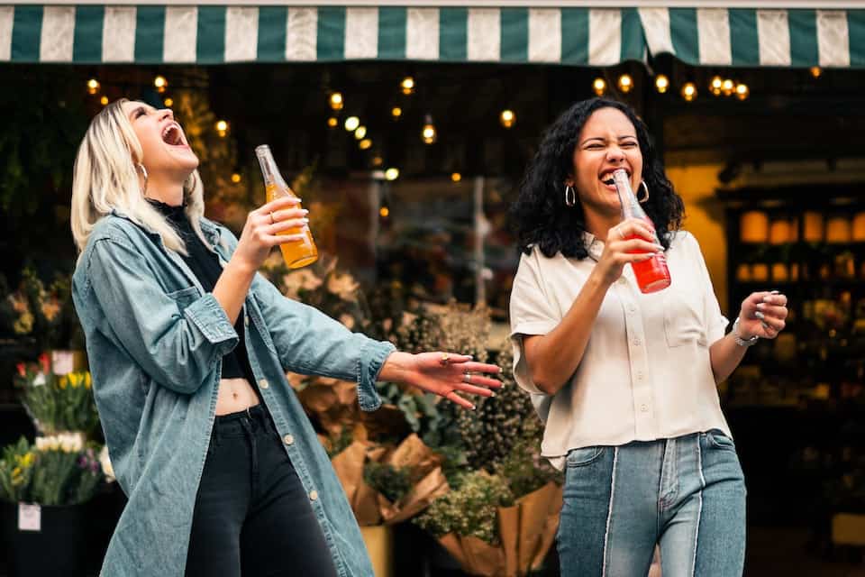 Two women smiling drinking soda from a bottle