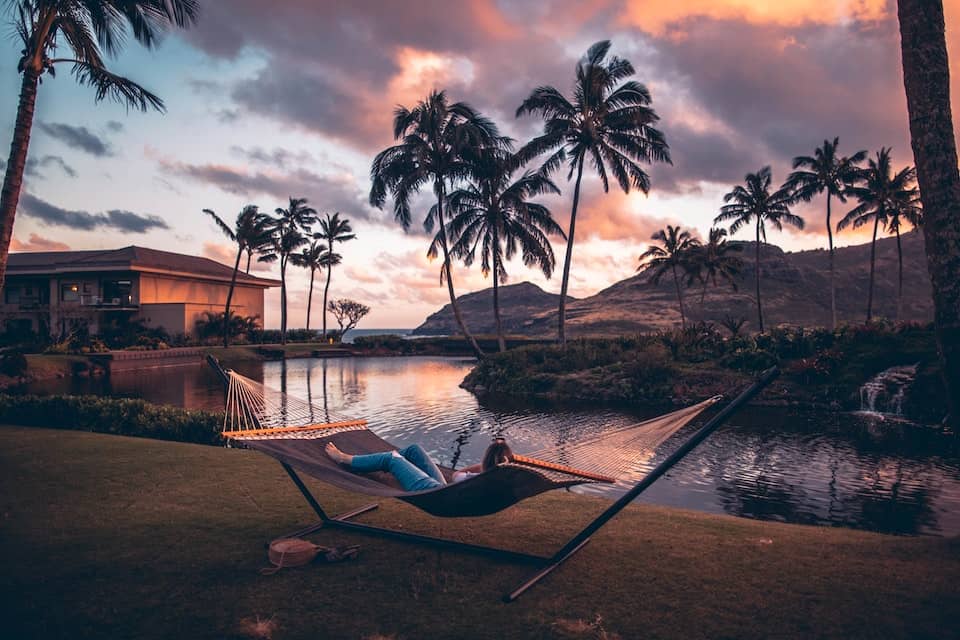 A woman laying on a hammock in front of palm trees enjoying summer relaxation